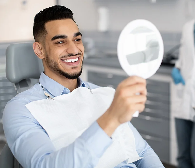 Happy Handsome Arab Man Looking To Mirror After Teeth Treatment In Clinic Lumineers Calgary