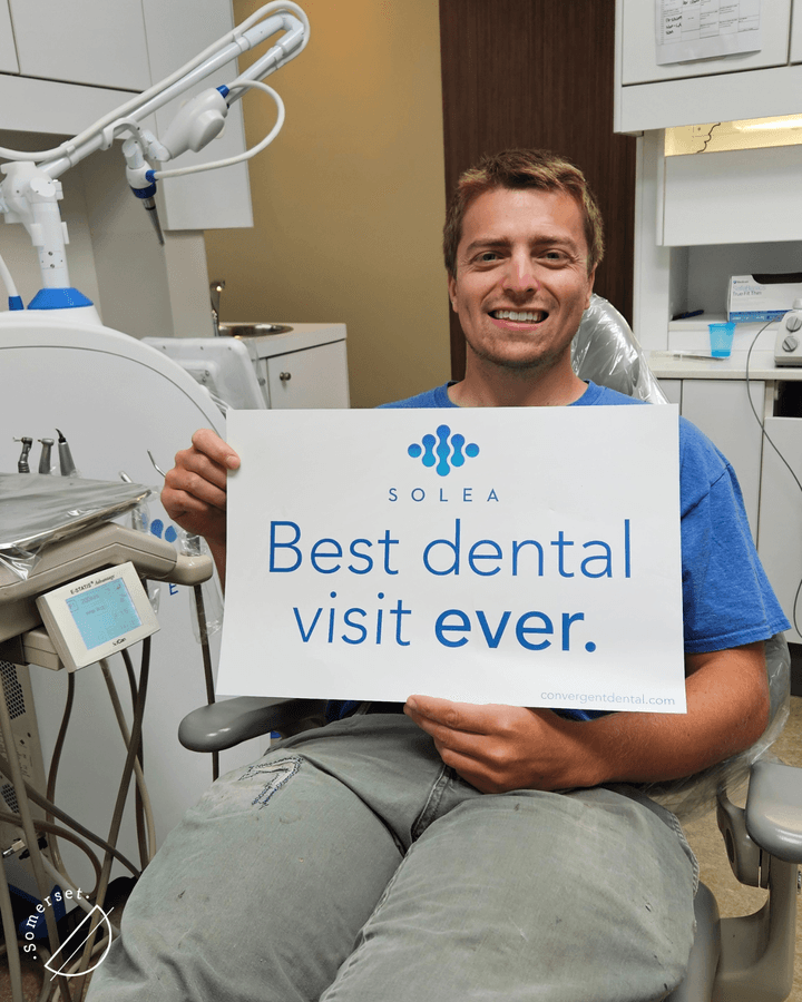 Smiling male patient holding “Best dental visit ever” sign after anxiety-free Solea laser treatment in SW Calgary. Smiling male patient holding "Best dental visit ever" sign after anxiety-free Solea laser treatment in SW Calgary.