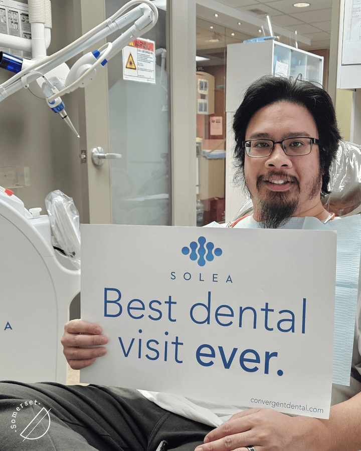 Satisfied patient with glasses holding sign praising comfortable laser dentistry experience at Calgary dental clinic. Satisfied patient with glasses holding sign praising comfortable laser dentistry experience at Calgary dental clinic.